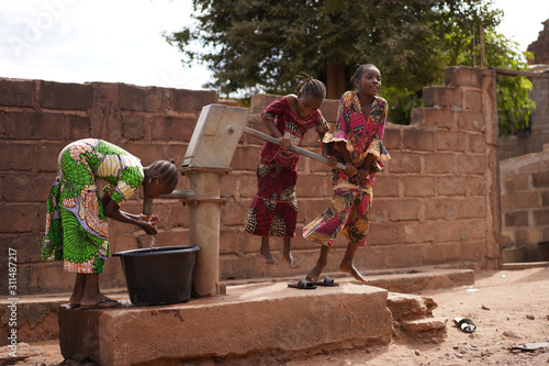 Three African Girls Showing Off Teamwork Skills Collecting Water At a Borhole Hand Pump