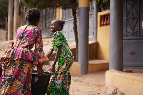 Two African Girls Carrying A Heavy Water Bucket Home From The Pumping Station