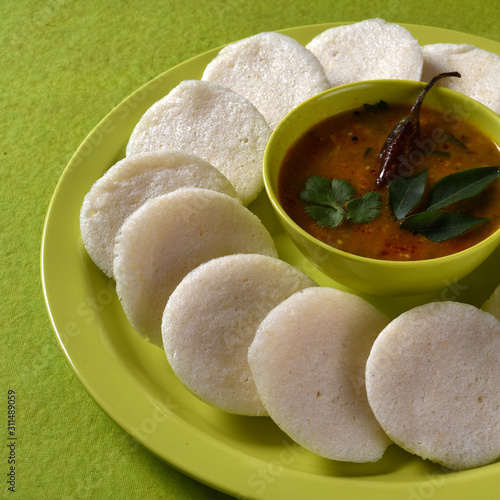 Idli with Sambar in bowl on green background, Indian Dish : south Indian favourite food rava idli or semolina idly or rava idly, served with sambar and green coconut chutney. photo