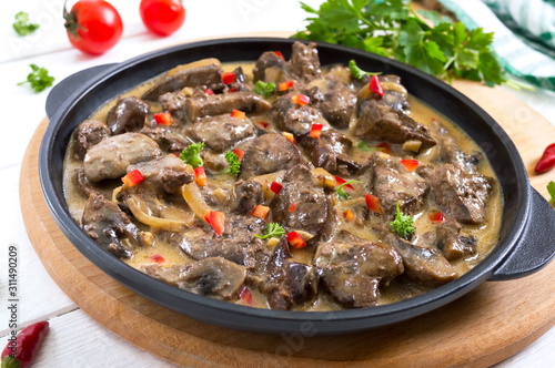 Turkey liver with onions and mushrooms in a creamy sauce on a white wooden background. Diet menu