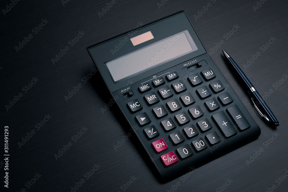 Top view on black accounting calculator and pen on a dark wooden office desk with copy space. Profit analysis, calculation of taxes and payments concept Top view on black accounting calculator and pen on a dark wooden office desk with copy space. Profit analysis, calculation of taxes and payments concept