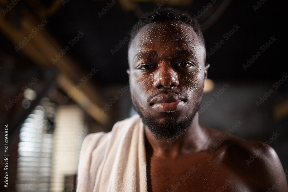 Portrait of African young shirtless man with towel on his shoulder looking at camera after training in gym Portrait of African young shirtless man with towel on his shoulder looking at camera after training in gym