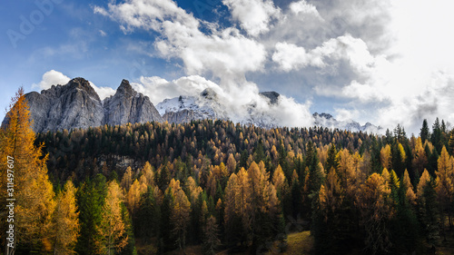 Colourful forest and Dolomite mountains surrounded by clouds in South Tyrol, Italy /View from Lago di Sorapis hiking trail / High ISO image