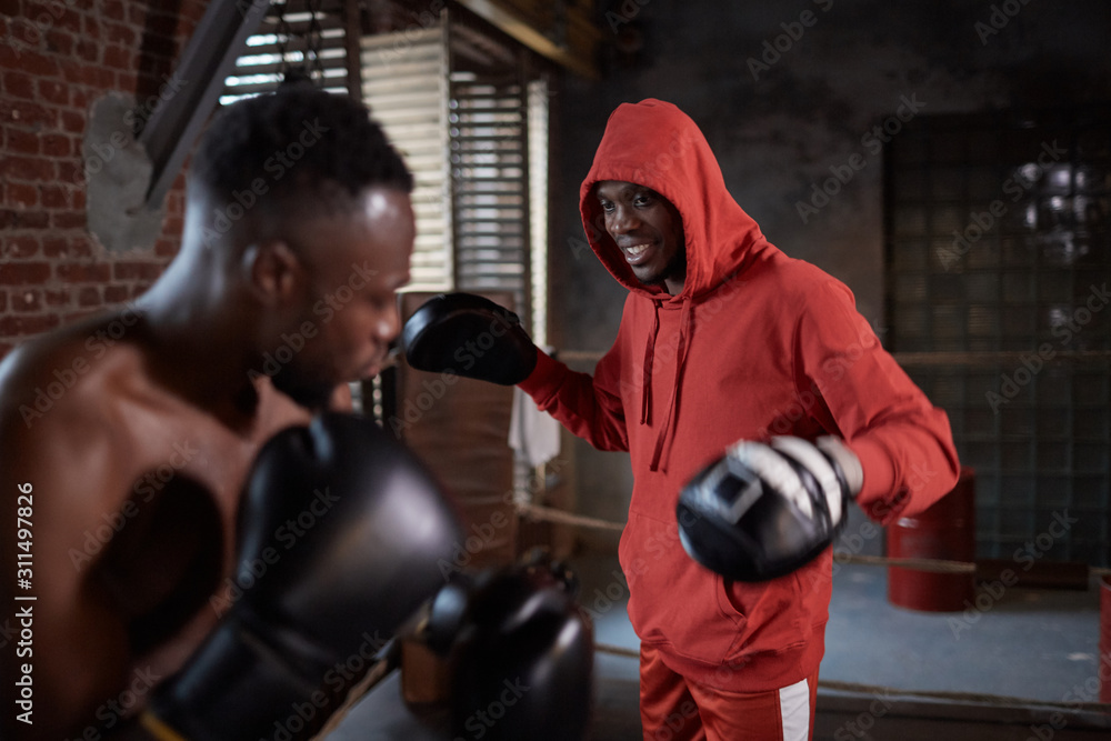 Two African sportsmen in boxing gloves fighting with each other in gym Two African sportsmen in boxing gloves fighting with each other in gym