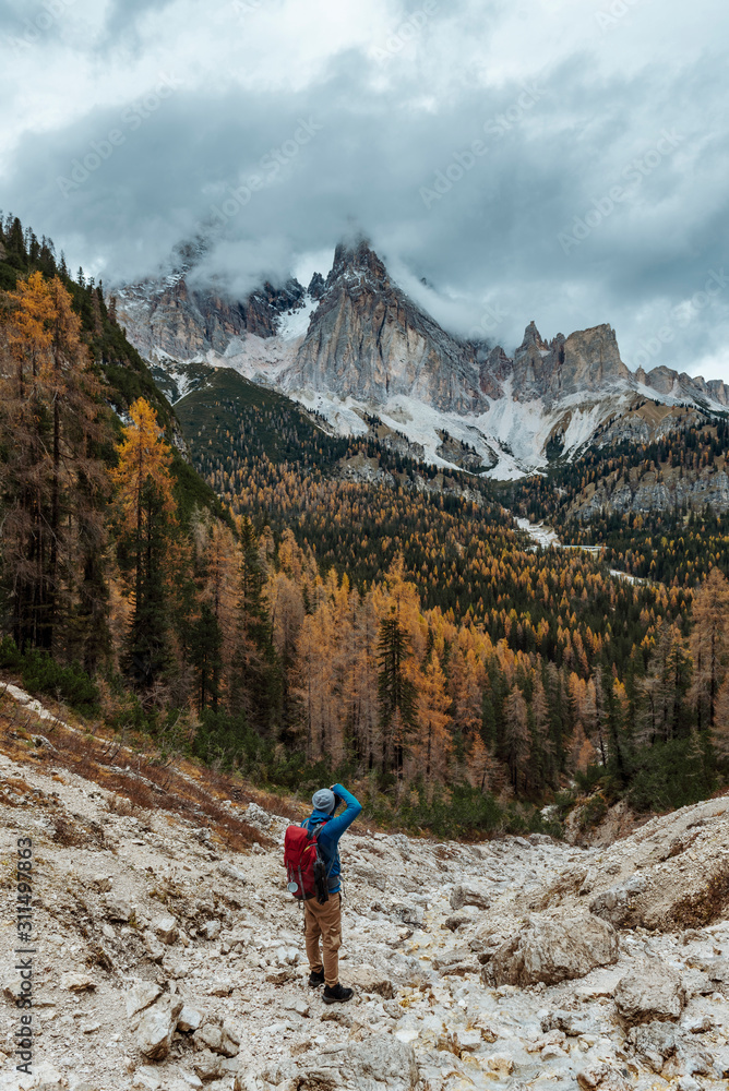 Young male dressed in colourful jacket standing on the ''lago di sorapis'' trail in Italian alps /  Dolomite mountains in background during sunset / High ISO image
