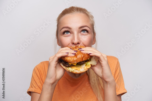 Leinwand Poster Portrait of pleased young lovely blonde woman with casual hairstyle eating fresh