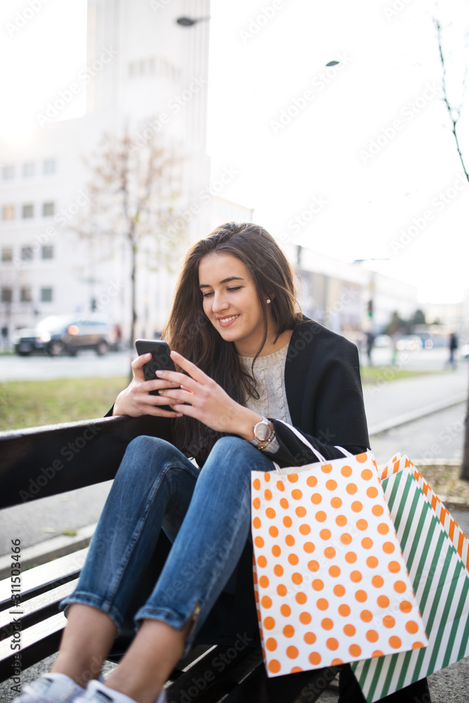 Fototapeta premium Beautiful woman siting on a bench and typing a message