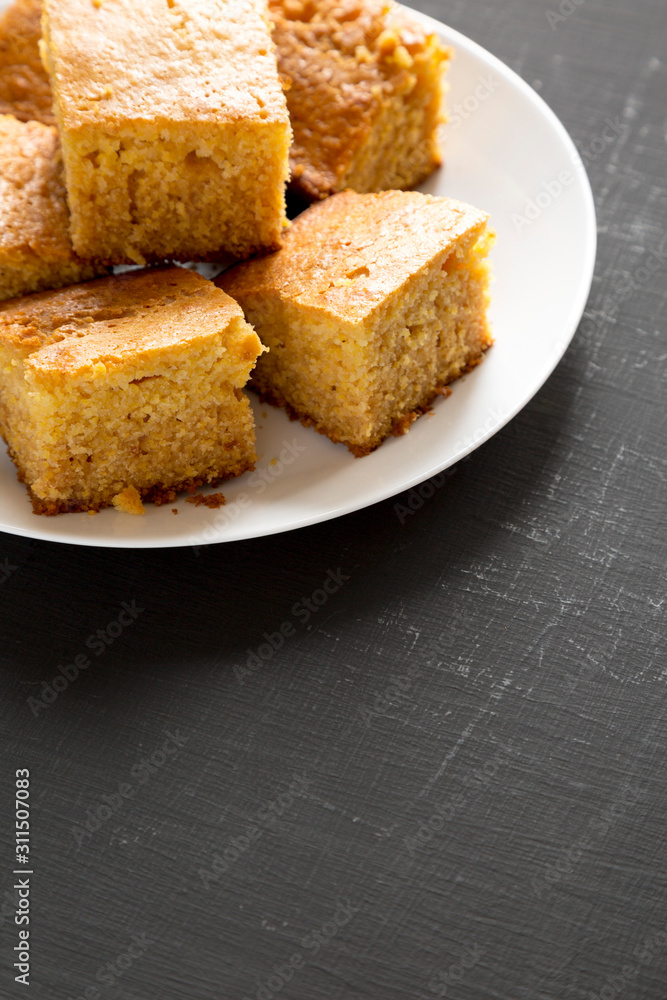 Homemade Sliced Cornbread Ready to Eat on a white plate on a black background, side view. Copy space.