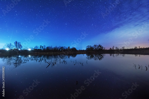 A magical starry night on the river bank with a large tree and a milky way in the sky and falling stars in the summer.  © reme80