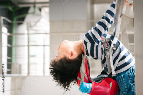 Little Asian hyperactive difficult boy hold handrail and lean body and head backwards, carry red backpack and insulated water bottle due to Autism, Behavioral and Attention Deficit Disorder.