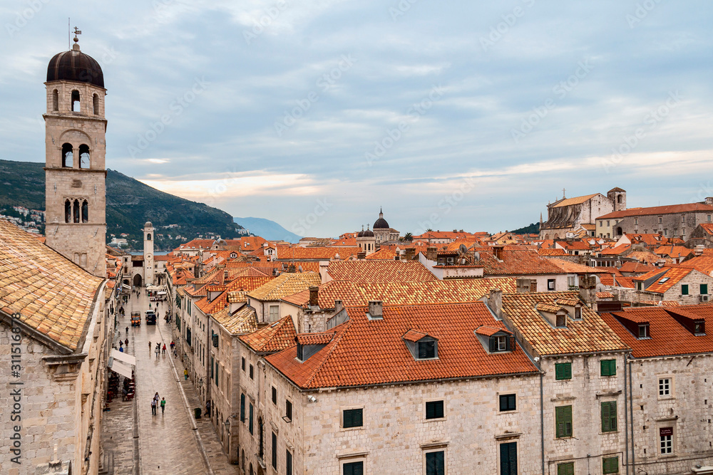 Croatian city of Dubrovnik with narrow streets and red tiled roofs against the backdrop of mountains and cloudy sky