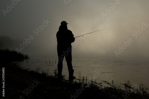 silhouette of a fisherman on the river in the fog