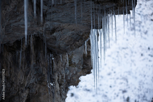 Icicles hang from a cliff. Long transparent and beautiful icicles on stones.