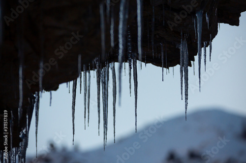 Icicles hang from a cliff. Long transparent and beautiful icicles on stones.