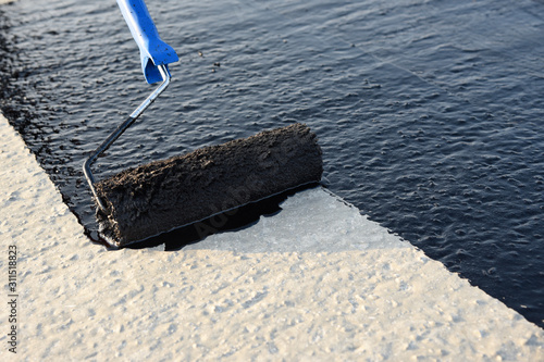 Worker applies bitumen mastic on the foundation photo