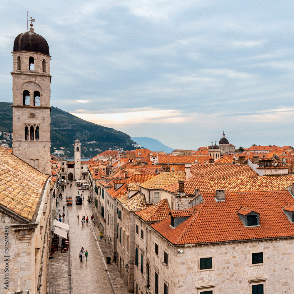 Croatian city of Dubrovnik with narrow streets and red tiled roofs against the backdrop of mountains and cloudy sky