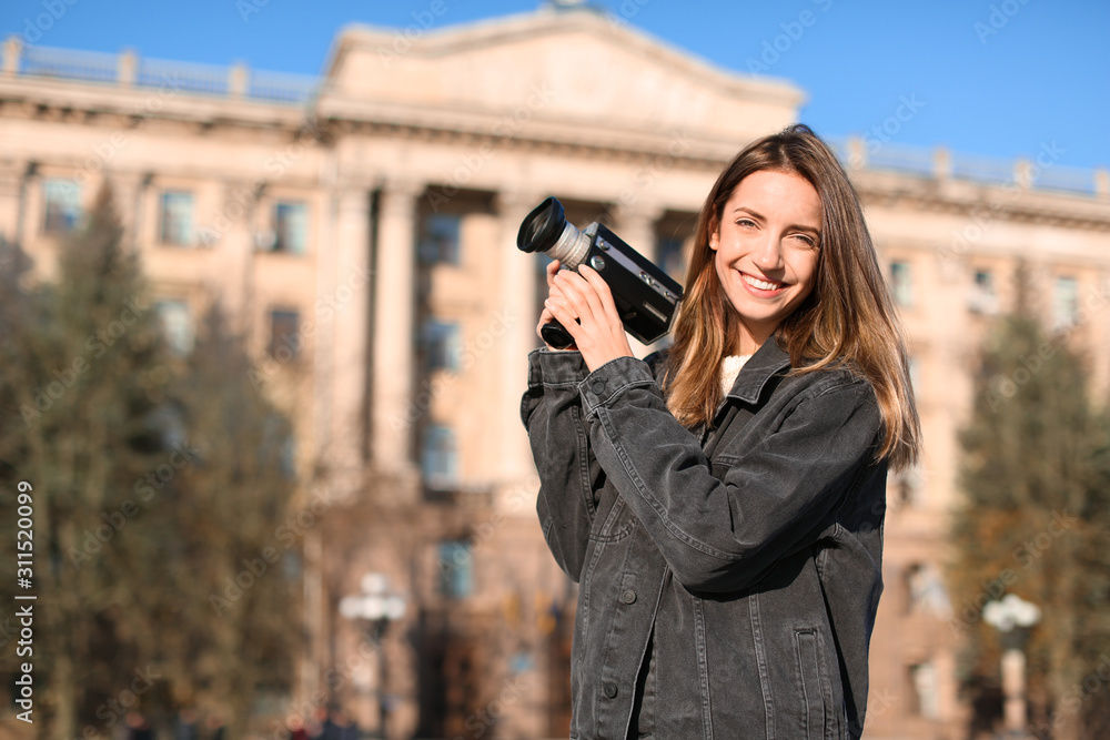 Beautiful young woman with vintage video camera on city street