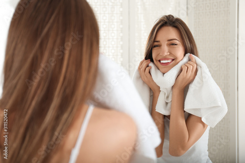 Young woman wiping face with towel near mirror in bathroom