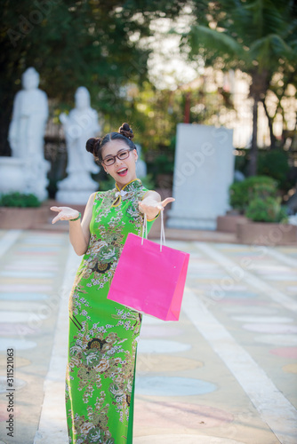 Action an Asian woman portrait of a beautiful smiling in wearing Cheongsam green dress with colorful shopping bags 