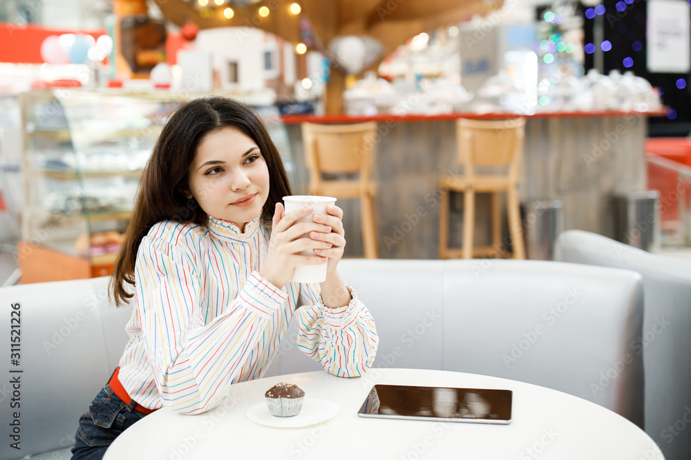Pretty young brunette girl sitting in cafe and holding tablet, drinking coffee and resting Pretty young brunette girl sitting in cafe and holding tablet, drinking coffee and resting