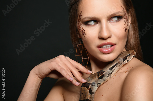 Beautiful woman with boa constrictor on black background, closeup