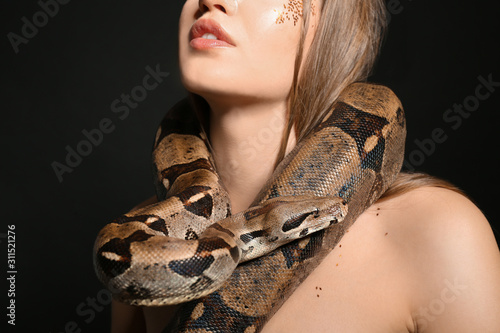 Beautiful woman with boa constrictor on black background, closeup