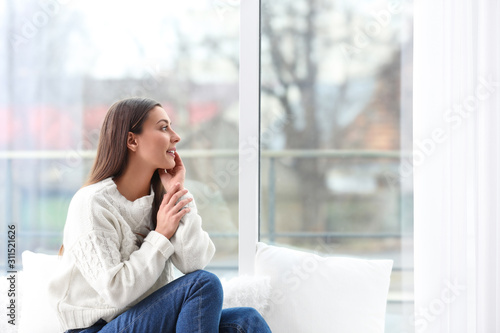 Tableau sur toile Young woman in sweater sitting near window indoors