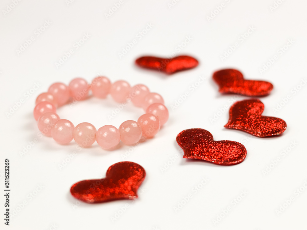 Rose quartz bracelet with red glitter hearts on white background. Valentine's day concept. Rose quartz bracelet with red glitter hearts on white background. Valentine's day concept.