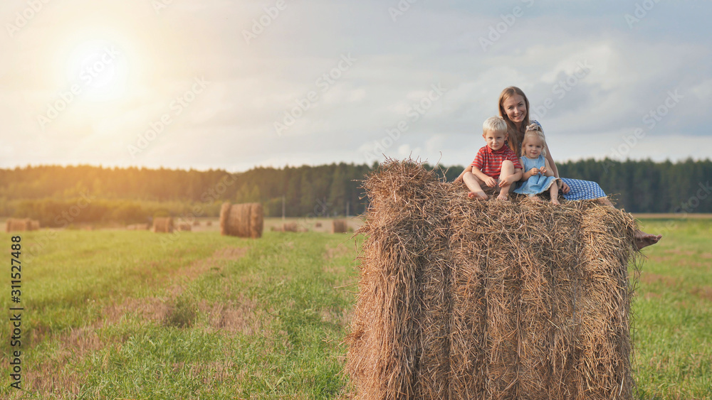 A mother with two children sits on a sheaf of straw in a field. A mother with two children sits on a sheaf of straw in a field.