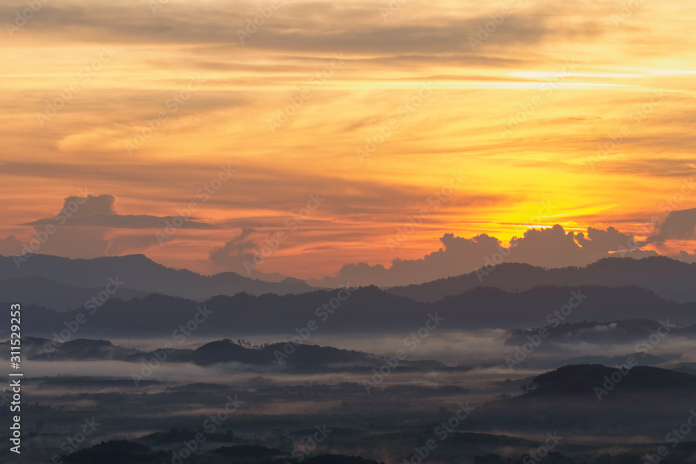 A morning view of a mist-covered mountain and the sun rising from the mountains.