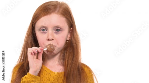 Close-up portrait shot of a lovely foxy haired girl with green eyes eating lollipop. Happy childhood concept