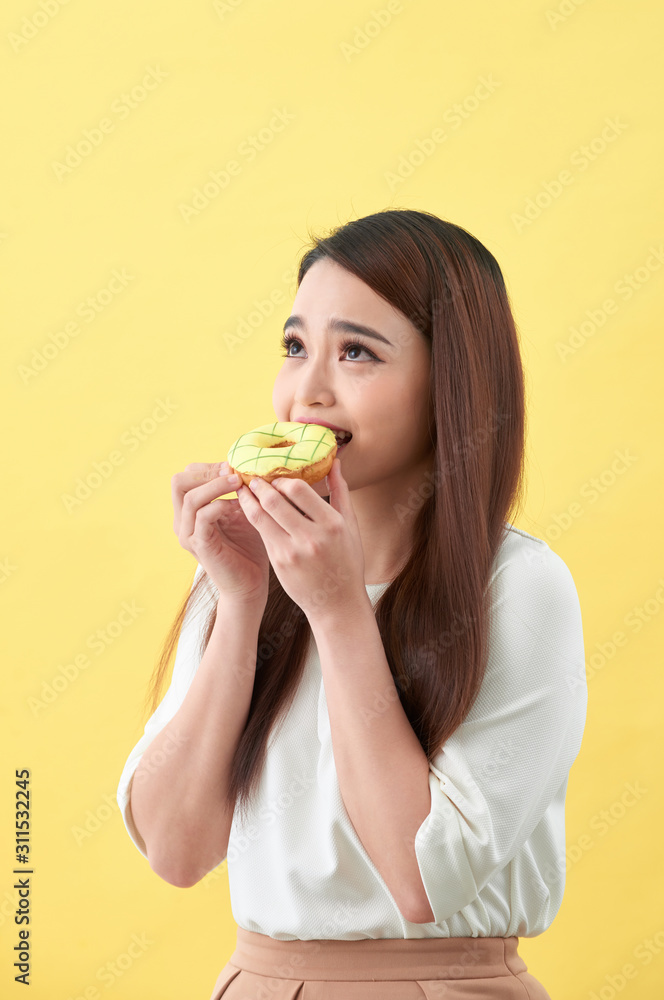 Close up portrait of a satisfied pretty girl eating donuts isolated over yellow background Close up portrait of a satisfied pretty girl eating donuts isolated over yellow background