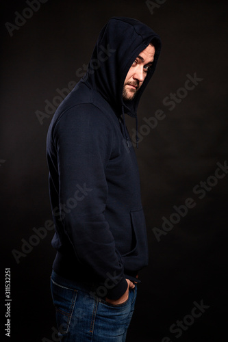A young man in a hoodie and hood on a black background. Danger and trouble. Vertical.