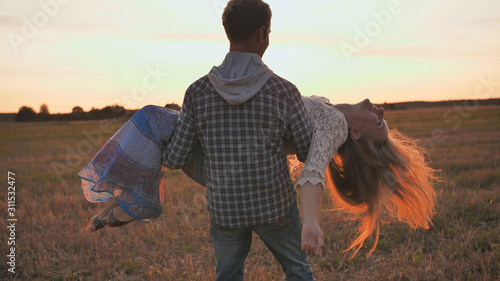 A guy is circling his girlfriend in his arms on a sunset background.