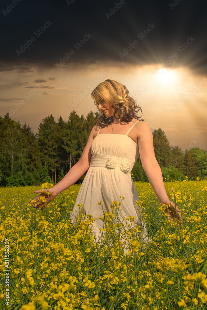 Fototapeta premium a woman with white dress in a rapsfield with dramatic sky