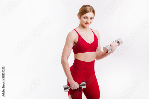 Young strong and sporty woman in red cloth doing exercises with dumbbells on white background