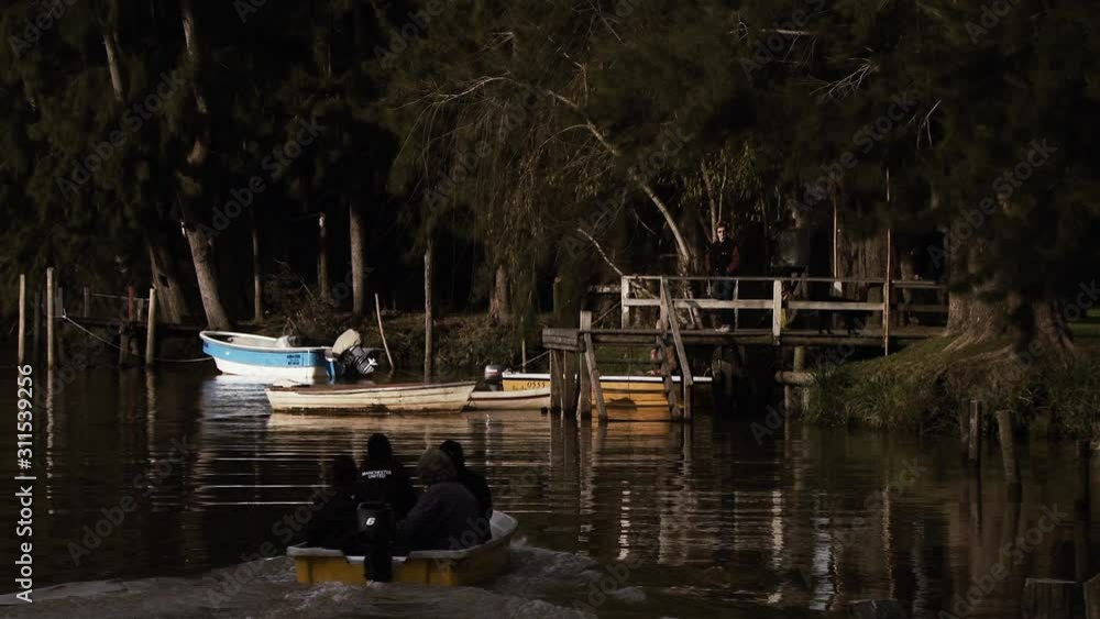 An Old Woman Driving A Small Motorboat With Her Family To A Rustic Quay. An Old Woman Driving A Small Motorboat With Her Family To A Rustic Quay.