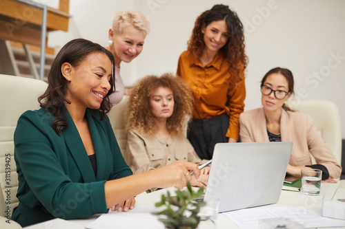 Group of five attractive female office workers watching something on laptop during business meeting