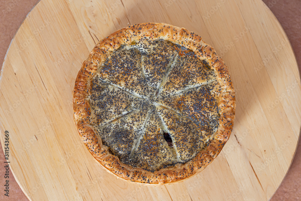A round french pastry salad pie with poppy seeds on a wooden round table.. From above. A round french pastry salad pie with poppy seeds on a wooden round table.. From above.