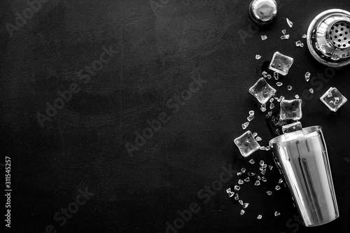 Bar utensil, tools - shaker, stainer - near ice cubes on black background top-down frame copy space