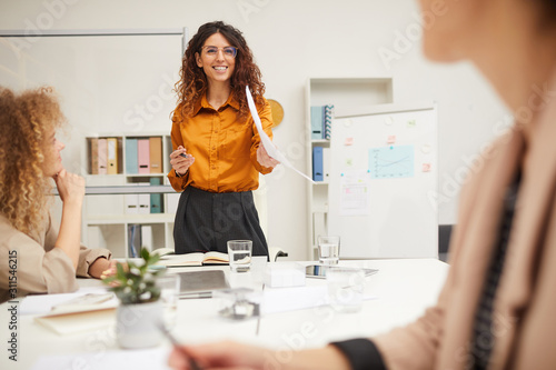 Attractive businesswoman with curly hair giving explanation of import of new business strategy at meeting, horizontal shot