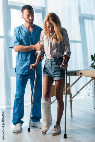 Photo handsome doctor looking at injured woman walking with crutches