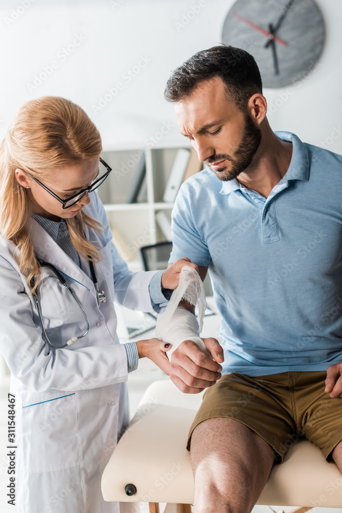 attractive orthopedist putting bandage on injured hand of handsome man attractive orthopedist putting bandage on injured hand of handsome man