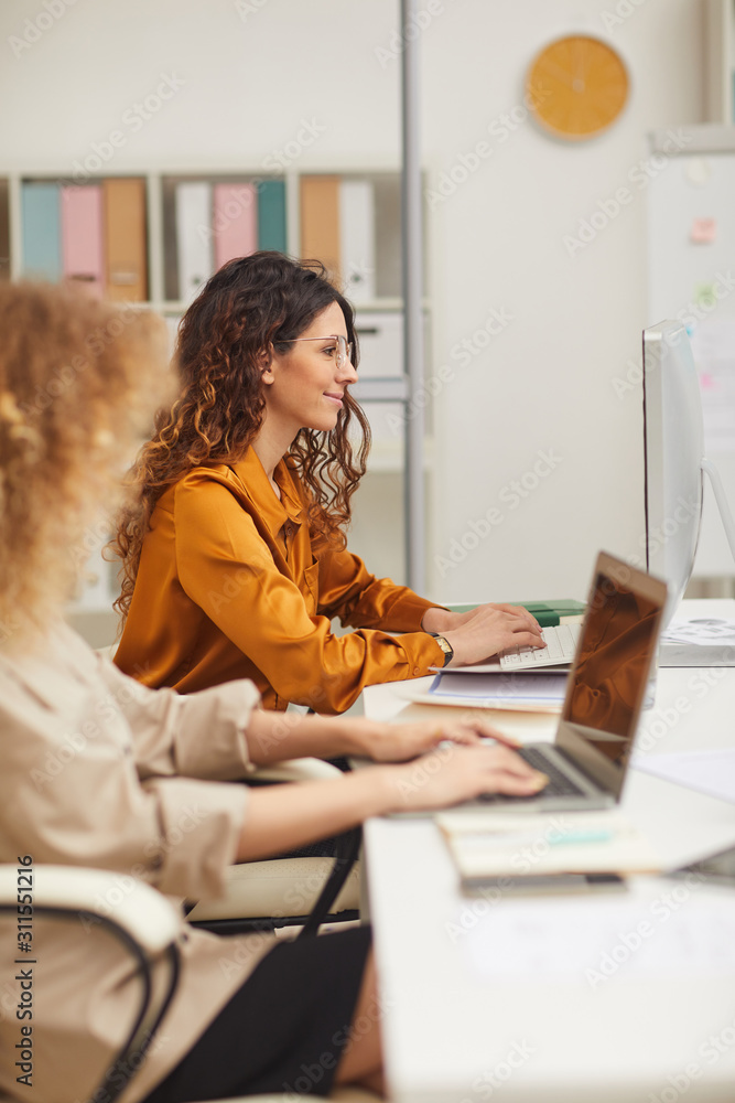 © Seventyfour - Women working on computers in modern office vertical side view shot