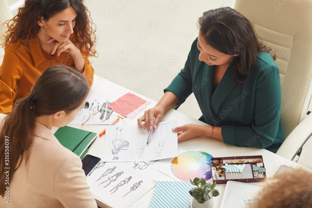 Group of young women working on fashionable clothes design together horizontal high angle shot Group of young women working on fashionable clothes design together horizontal high angle shot