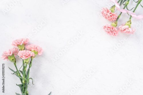 Beautiful, elegant pink carnation flower over bright white marble table background, concept of Mother's Day flower gift, top view, flat lay, overhead