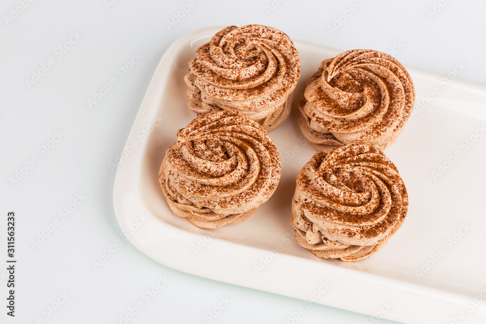 Four marshmallows, sprinkled with cinnamon and chocolate, lie on a white rectangular plate. Top view, on a white background.