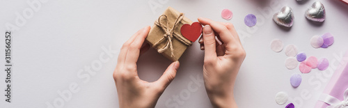 cropped view of woman holding valentines gift box with heart near decoration on white background, panoramic shot