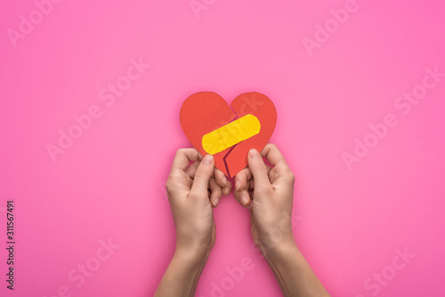 cropped view of holding broken paper heart with patch isolated on pink background