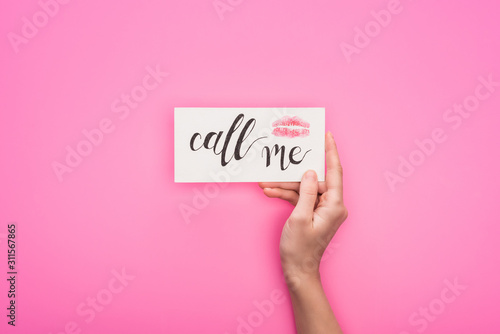 cropped view of woman holding card with lip print and call me lettering isolated on pink